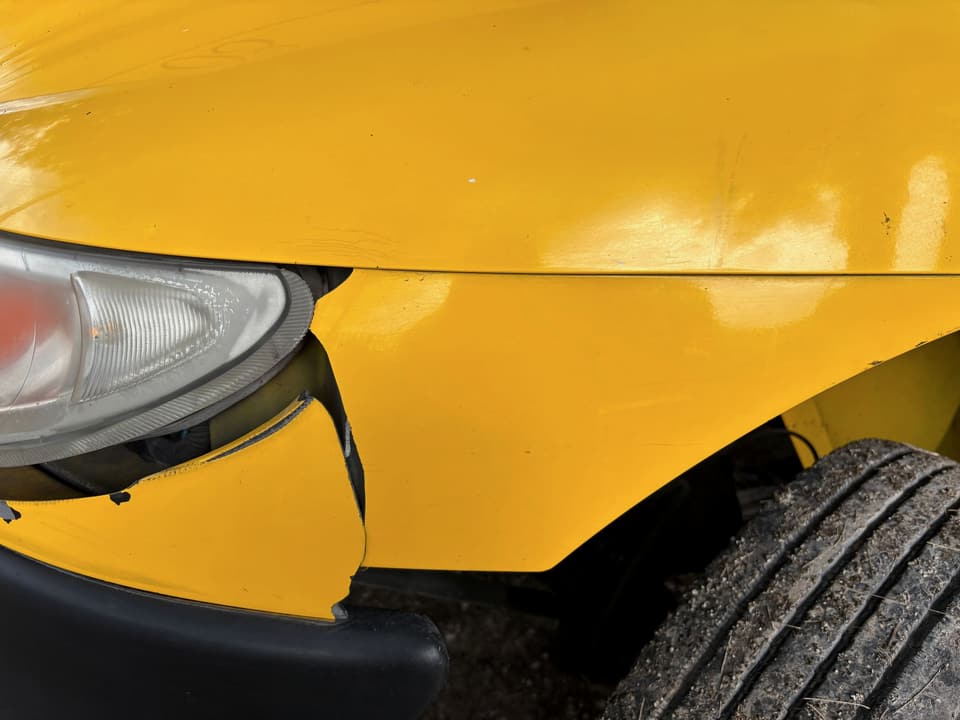 Close-up of a yellow car with a cracked front bumper and damaged guard