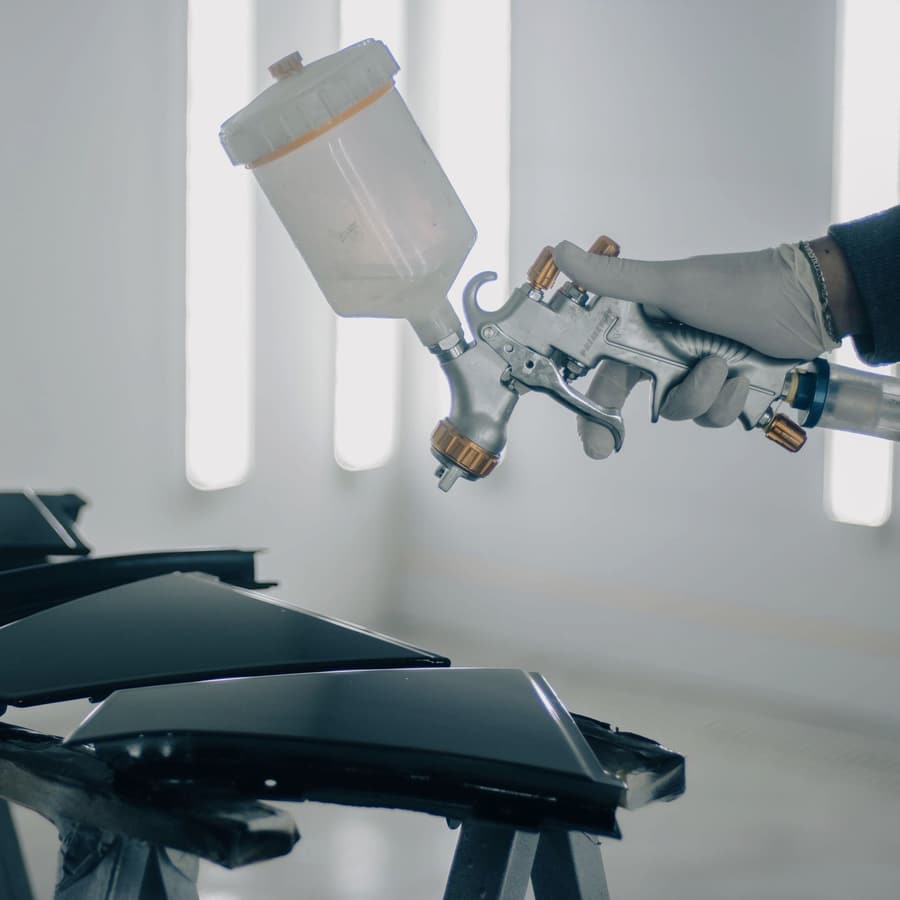 A spray gun held over freshly painted car panels in a spray booth